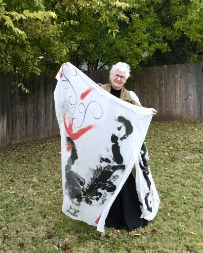 Artist holding an off-white shawl with a zen chicken printed on it.